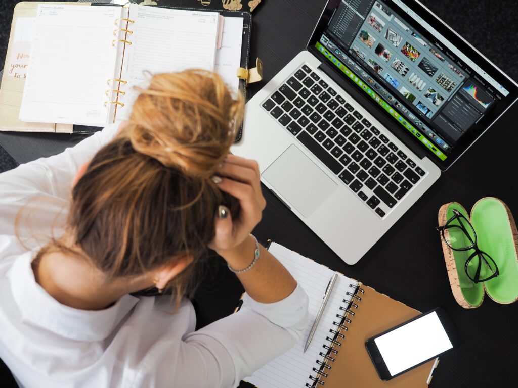 a woman who is setting at a desk with a computer and paperwork that is struggling